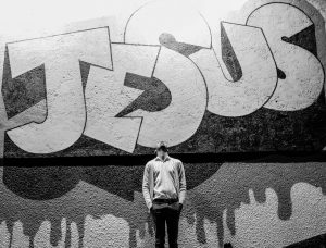 grayscale photography of a man standing in front of a Jesus graffiti