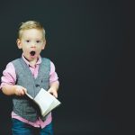 boy wearing gray vest and pink dress shirt holding book